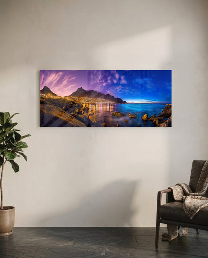 Glass wall art mounted on white wall showing twilight coastal city with illuminated mountains reflected in blue water.