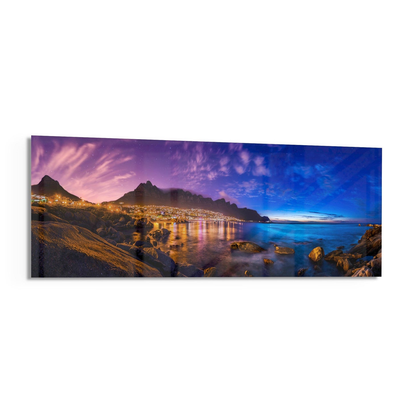 Twilight coastal cityscape with illuminated mountains, calm water, rocky foreground, and purple-to-blue gradient sky on glass wall art.