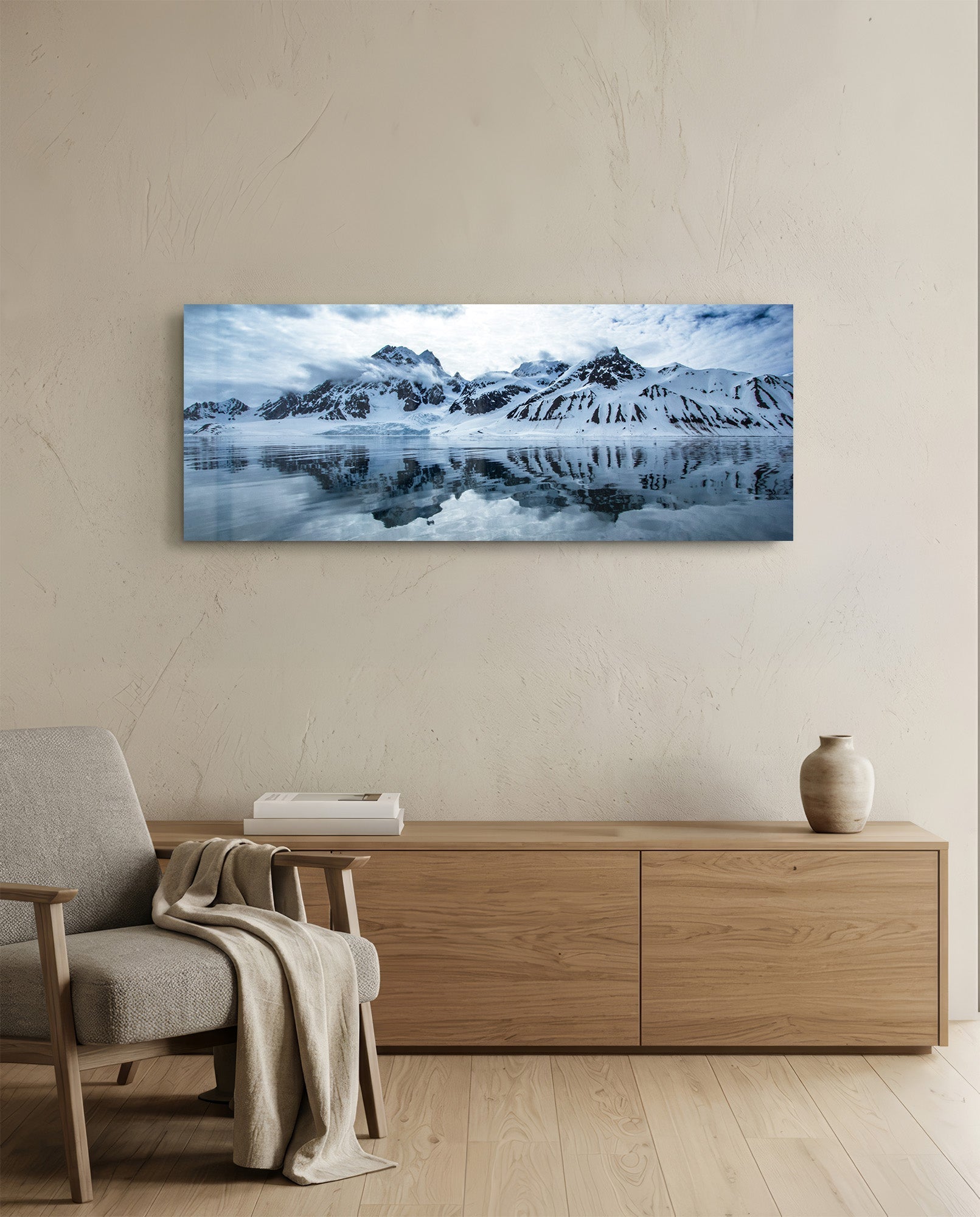 Snowy mountain landscape with blue sky and water reflections displayed as glass wall art above wooden dresser in minimalist interior.