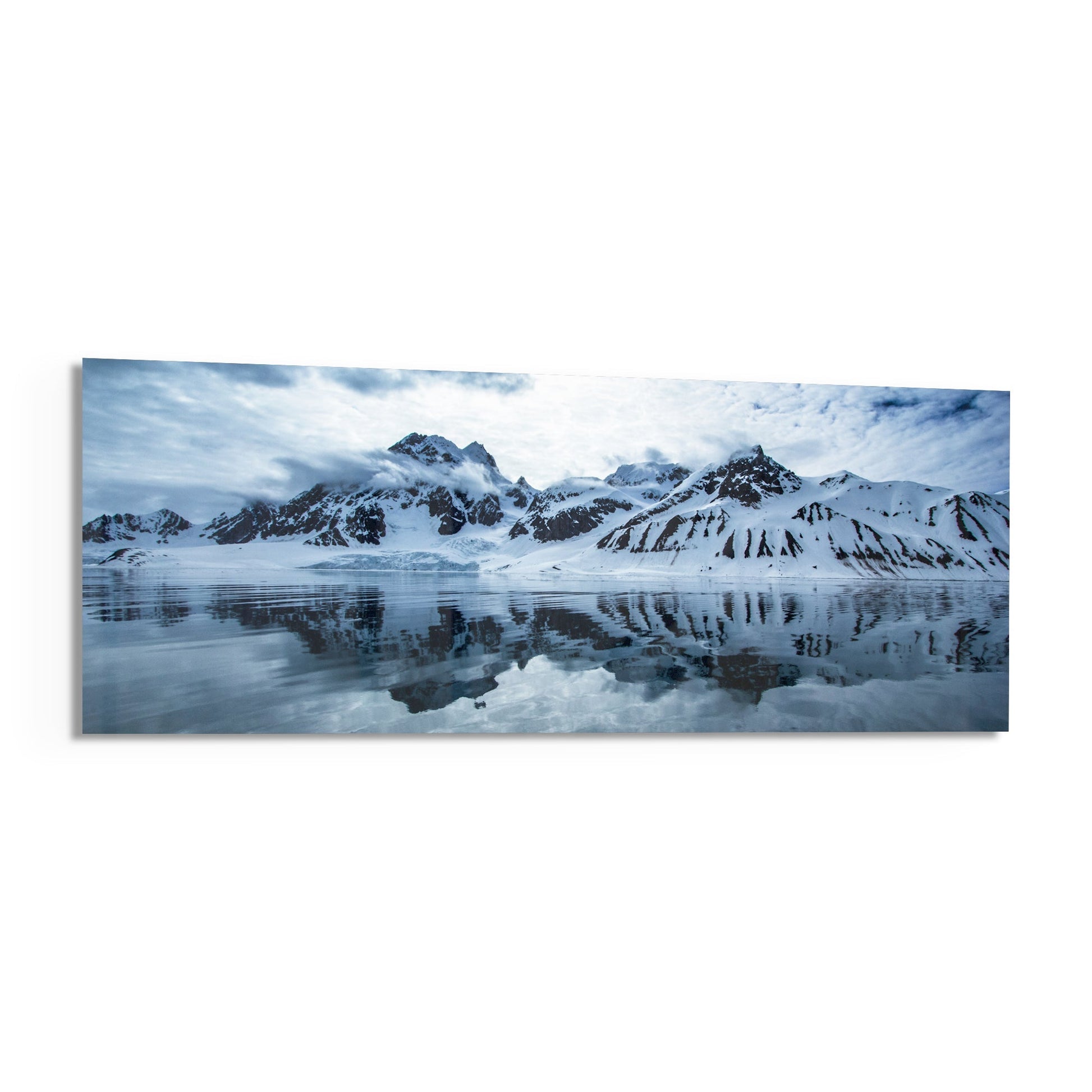 Panoramic glass wall art depicting snow-covered mountains reflected in still icy water under cloudy sky.