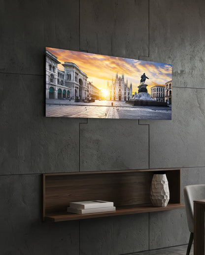 Horizontal glass wall art depicting Milan's Piazza Duomo at sunset, mounted above wooden shelf on concrete wall.