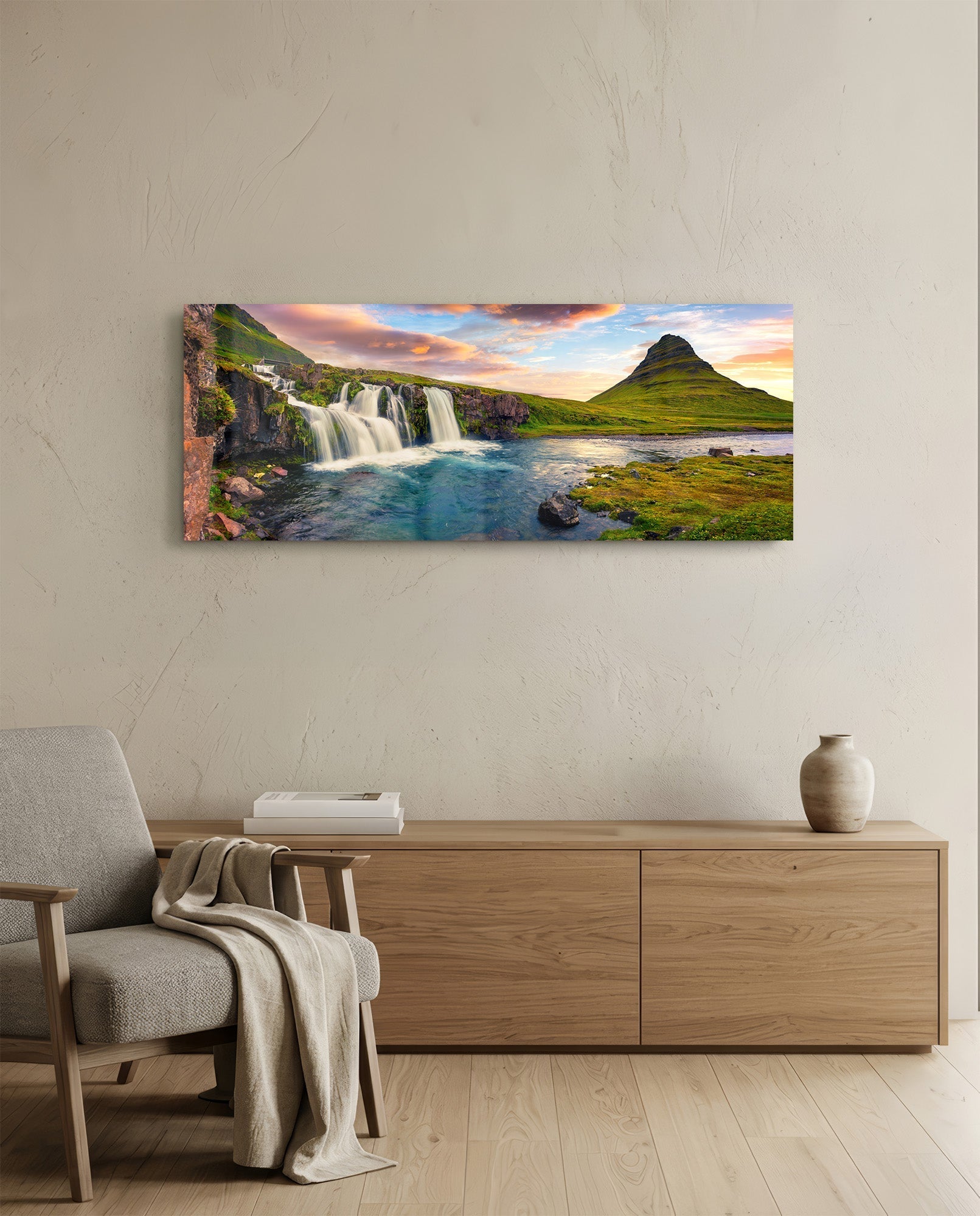 Waterfall glass wall art displaying Icelandic landscape with cascading waterfall, turquoise river, green mountain, and sunset sky, mounted above wooden dresser.