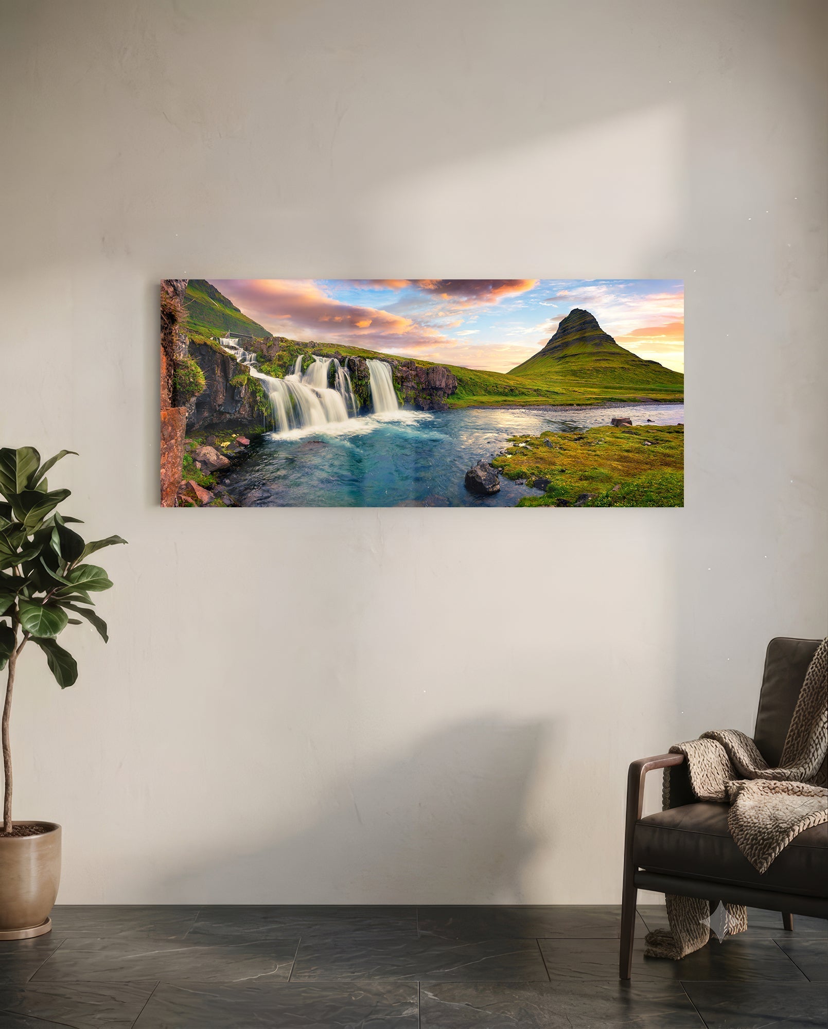 Rectangular glass wall art displaying Icelandic waterfall landscape with turquoise water, green mountains, and sunset sky, mounted on white wall above chair.