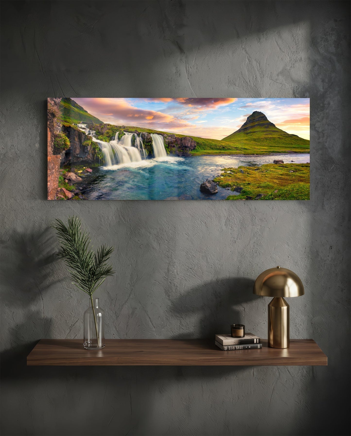 Horizontal glass wall art displaying Icelandic waterfall and mountain landscape at sunset, mounted above wooden shelf with decor.