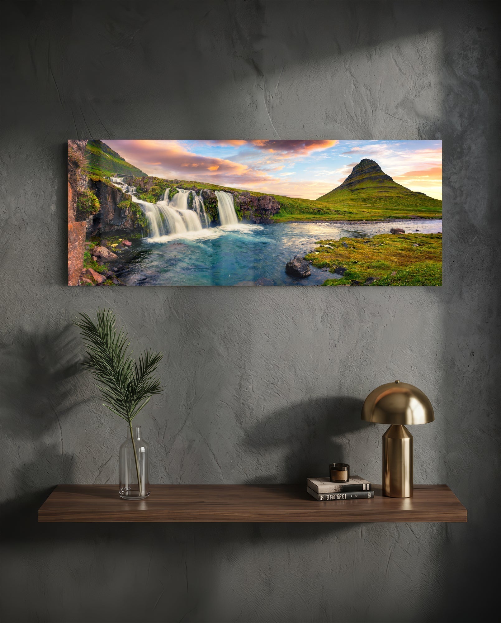Horizontal glass wall art displaying Icelandic waterfall and mountain landscape at sunset, mounted above wooden shelf with decor.