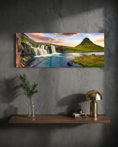 Horizontal glass wall art displaying Icelandic waterfall and mountain landscape at sunset, mounted above wooden shelf with decor.