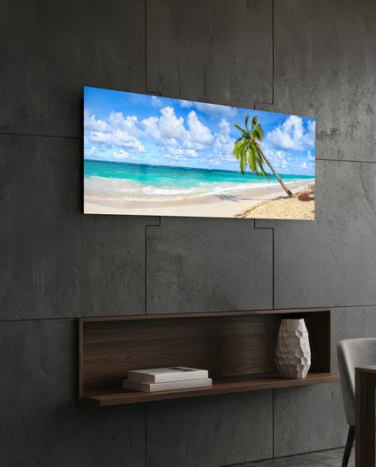 Tropical beach glass wall art displaying turquoise ocean and leaning palm tree mounted above wooden shelf on concrete wall.