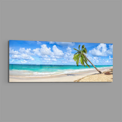 Panoramic glass wall art displaying a tropical beach scene with a leaning palm tree, turquoise water, white sand, and blue sky with white clouds.