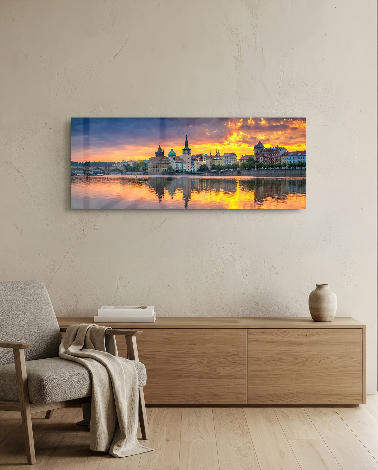 Prague Glass Wall Art displaying golden sunset over riverside cityscape with illuminated historic buildings reflected in water, hung above wooden dresser in modern room.