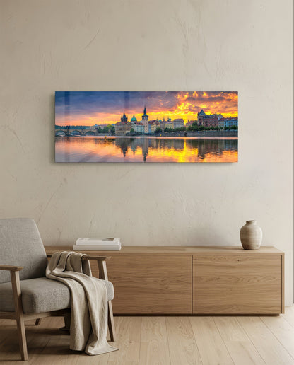 Prague Glass Wall Art displaying golden sunset over riverside cityscape with illuminated historic buildings reflected in water, hung above wooden dresser in modern room.