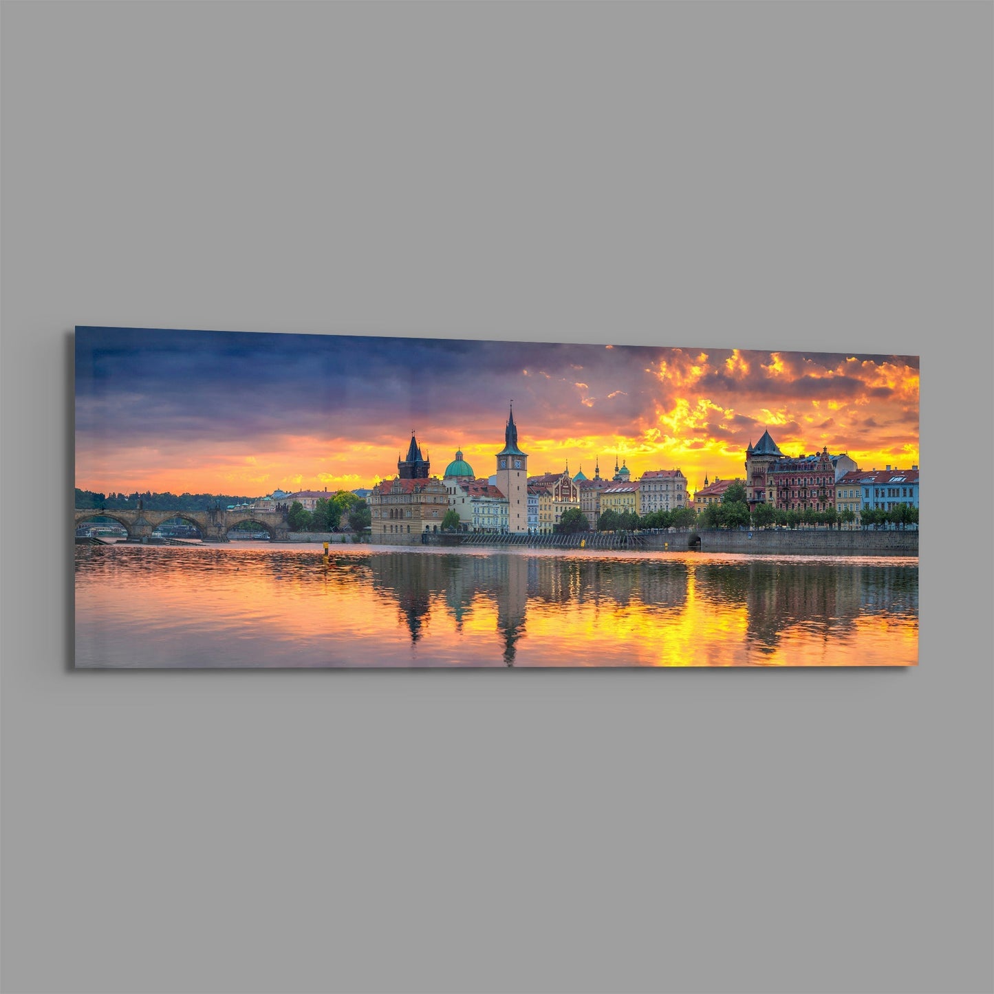 Panoramic glass wall art displaying Prague's riverside architecture at golden sunset with reflected light on water.