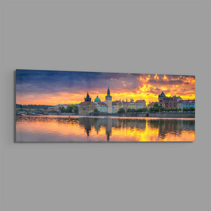 Panoramic glass wall art displaying Prague's riverside architecture at golden sunset with reflected light on water.