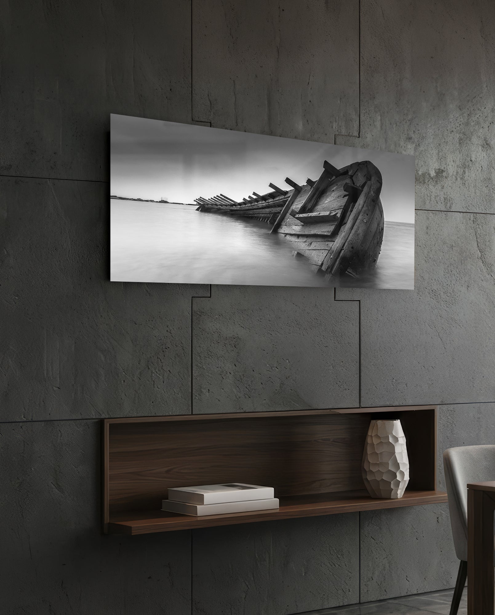 Black and white shipwreck photograph mounted on concrete wall above wooden shelf with books and decorative vase.