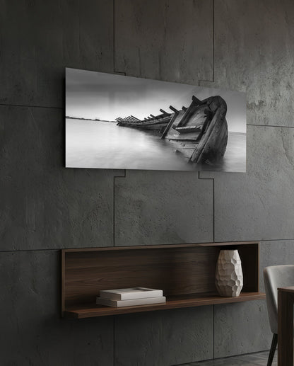 Black and white shipwreck photograph mounted on concrete wall above wooden shelf with books and decorative vase.