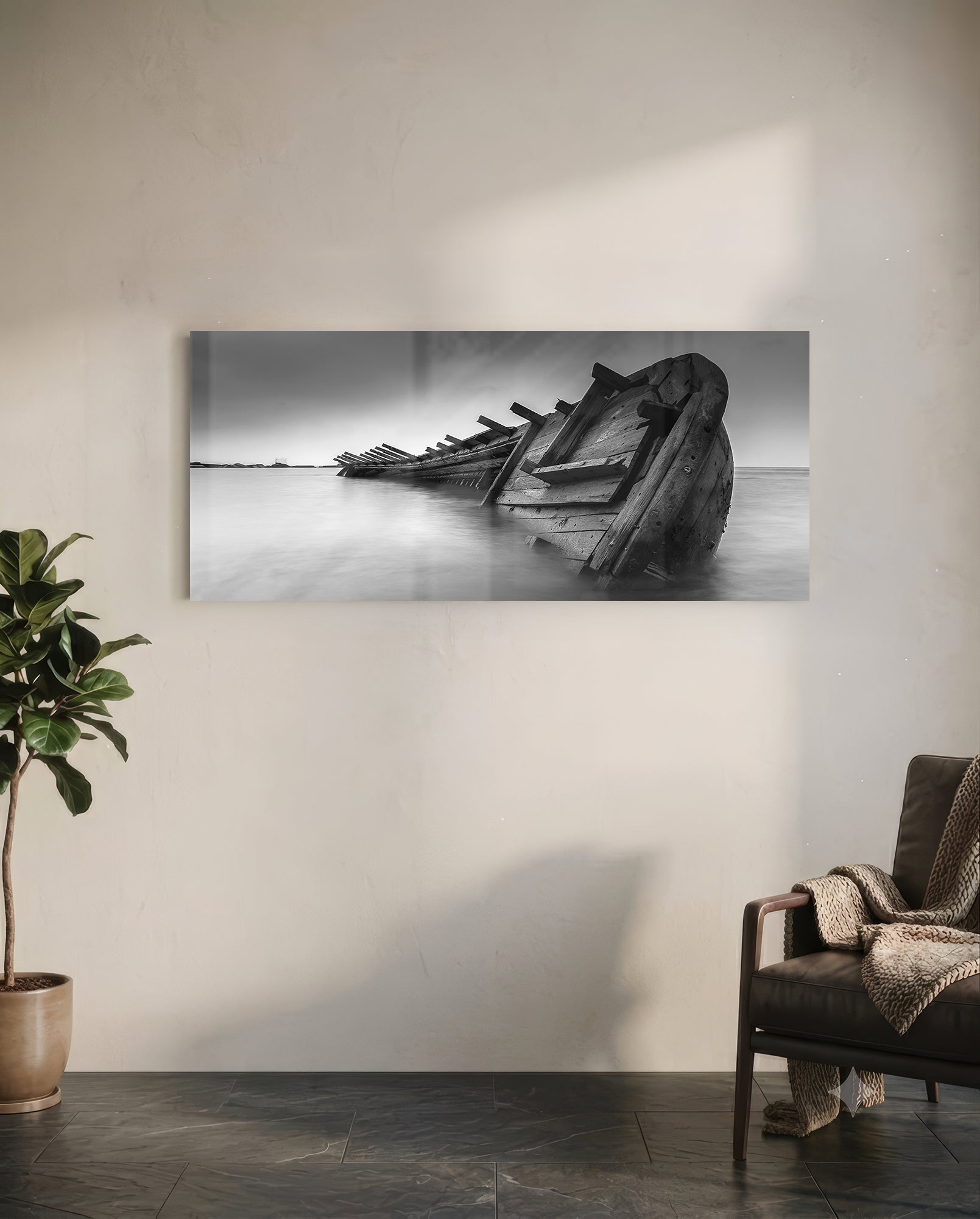 Black and white framed shipwreck glass art hanging on white wall above leather chair and potted plant.