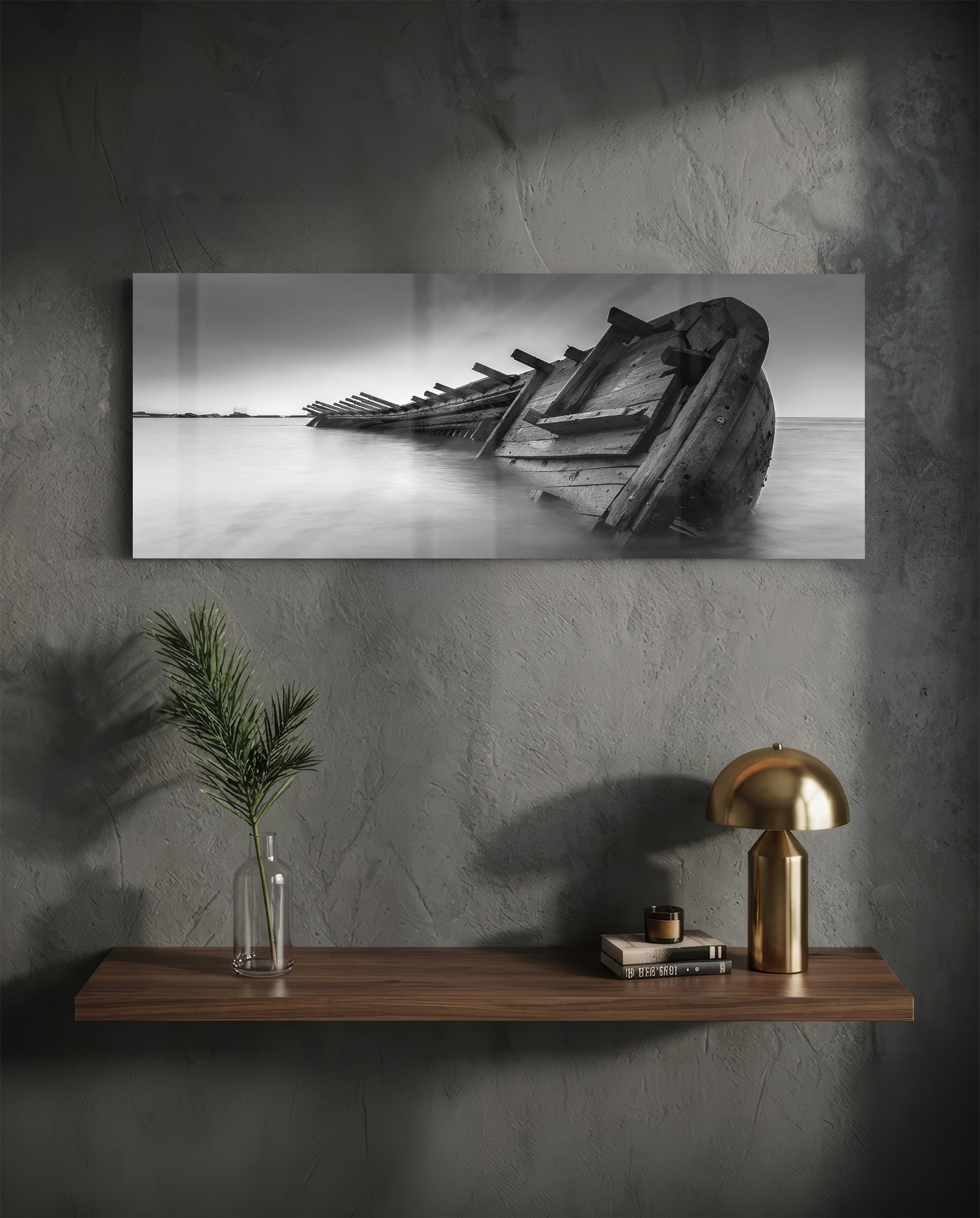 Black and white photograph of weathered shipwreck remains in shallow water, displayed as horizontal wall art above wooden shelf.