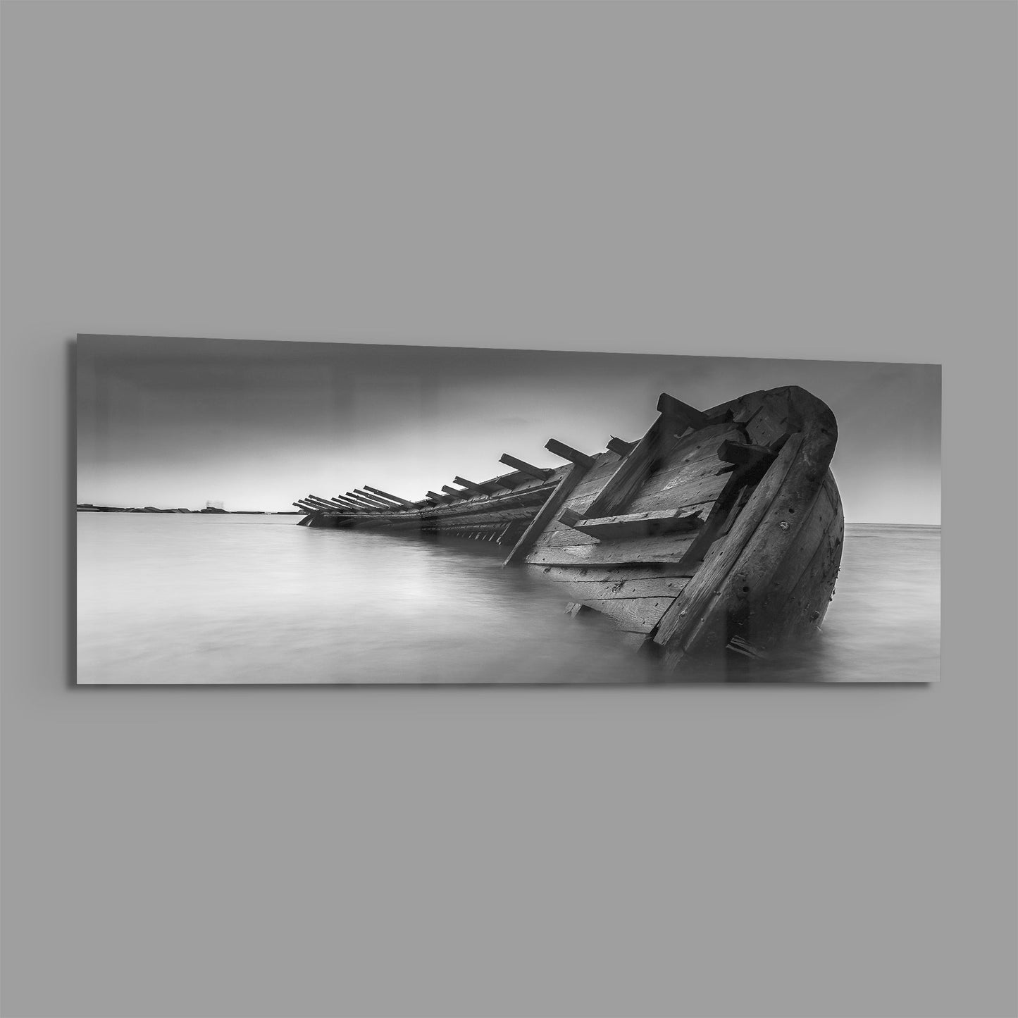 Black and white photograph of a deteriorated wooden shipwreck partially submerged in shallow water, mounted as horizontal glass wall art.