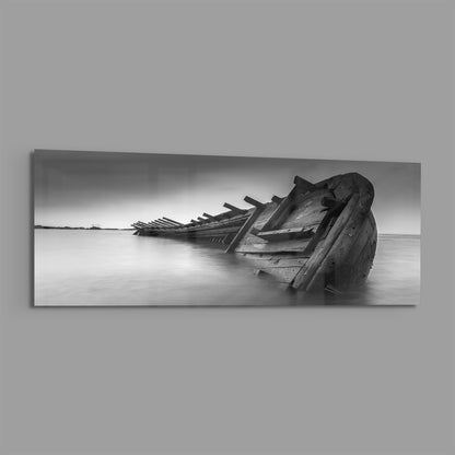 Black and white photograph of a deteriorated wooden shipwreck partially submerged in shallow water, mounted as horizontal glass wall art.