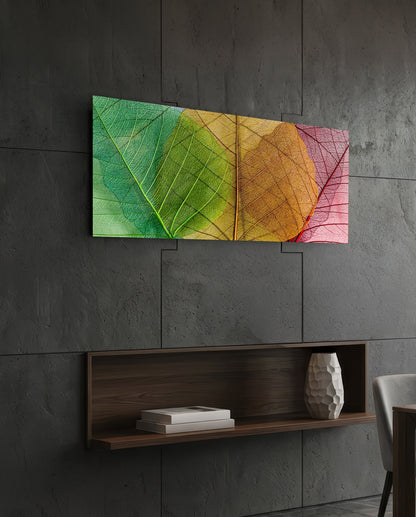 Colorful gradient glass wall art displaying overlapping leaf veins in green, yellow, orange, and pink tones, mounted on concrete wall above wooden shelf.