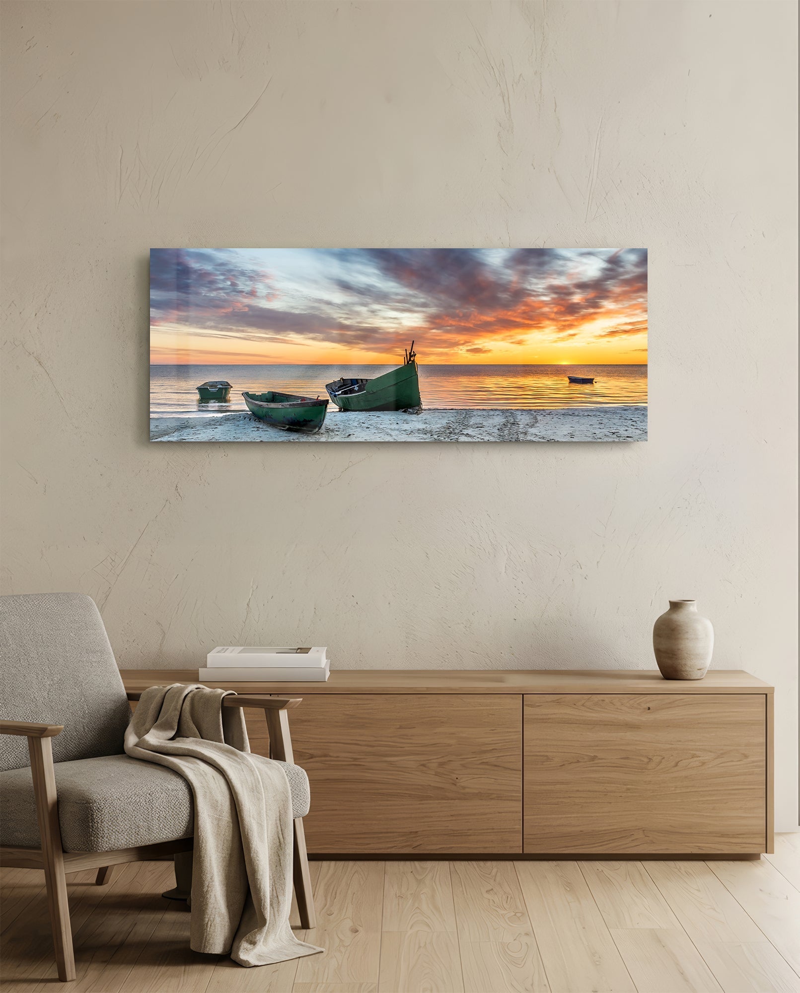 Glass wall art mounted above wooden dresser showing green fishing boats on beach at golden sunset with orange sky.