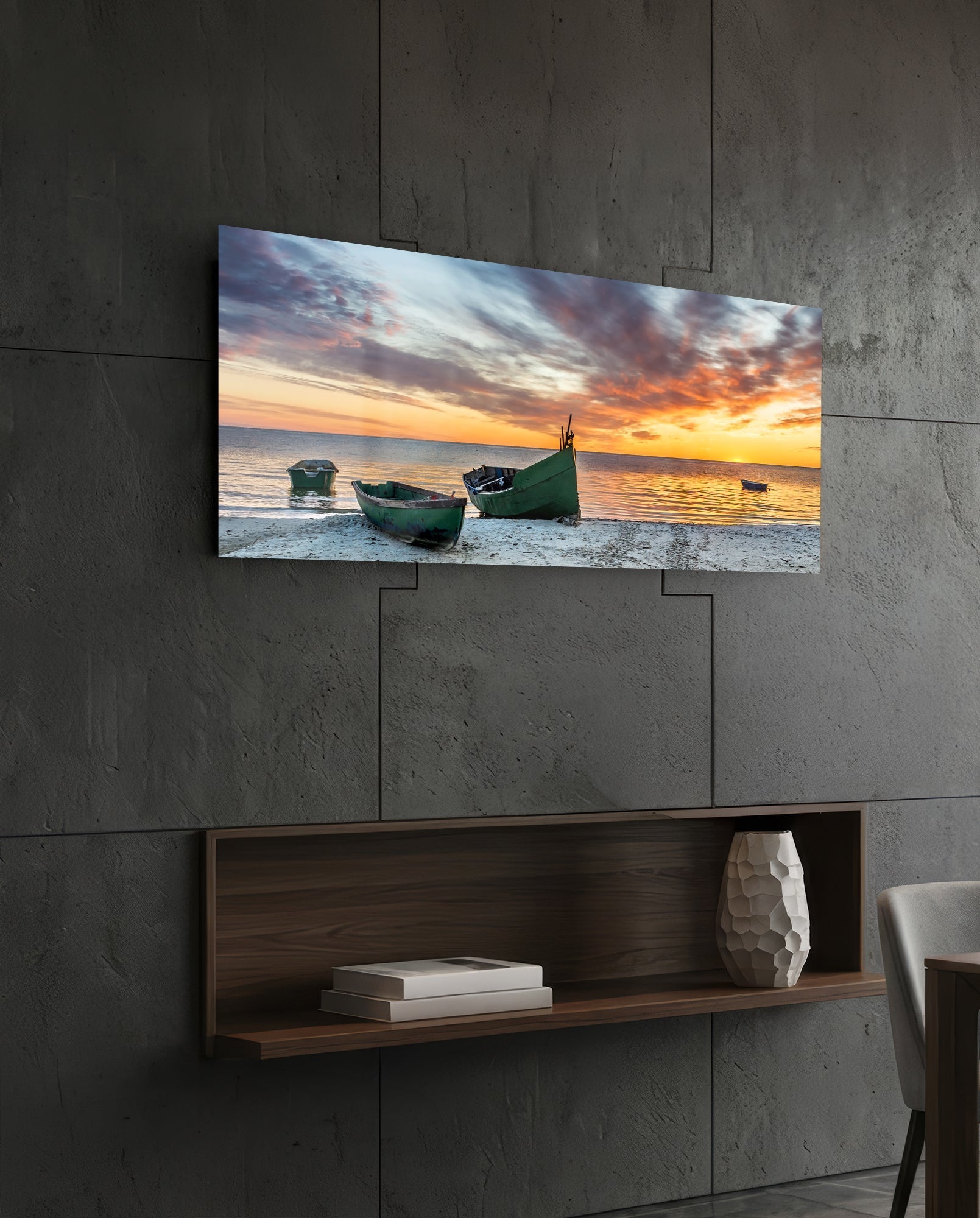 Glass wall art depicting three green fishing boats on a beach at sunset, mounted on a concrete wall above a wooden shelf.