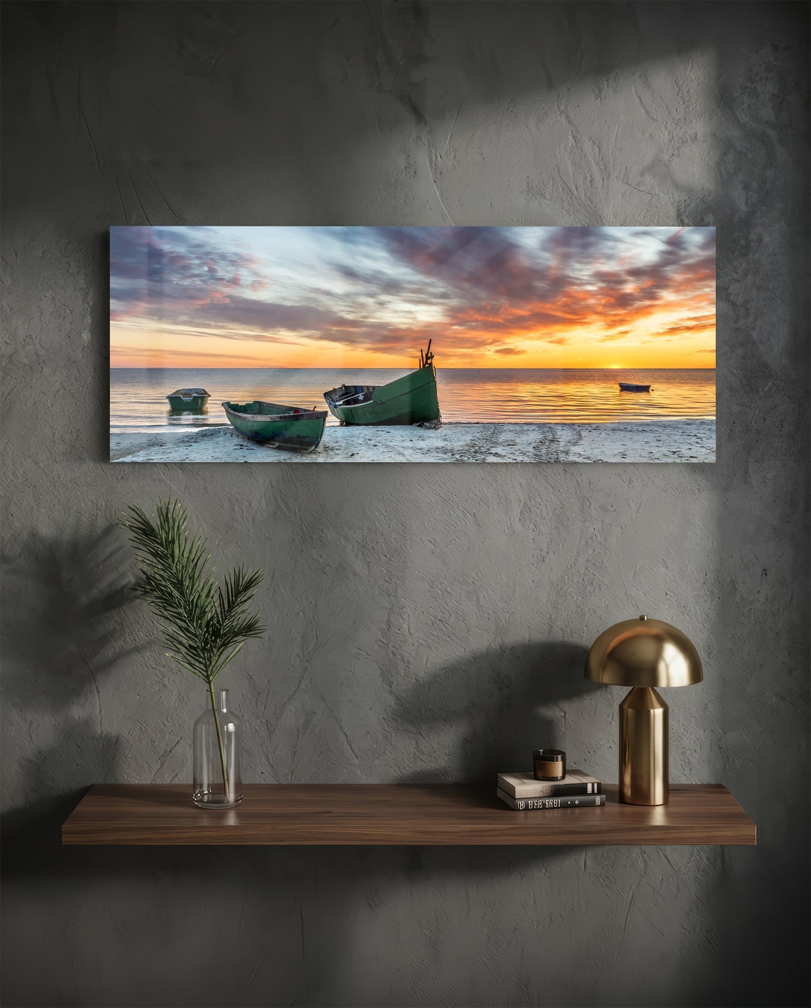 Horizontal glass wall art displaying three green fishing boats on a beach at sunset with golden and orange sky reflected in calm water.