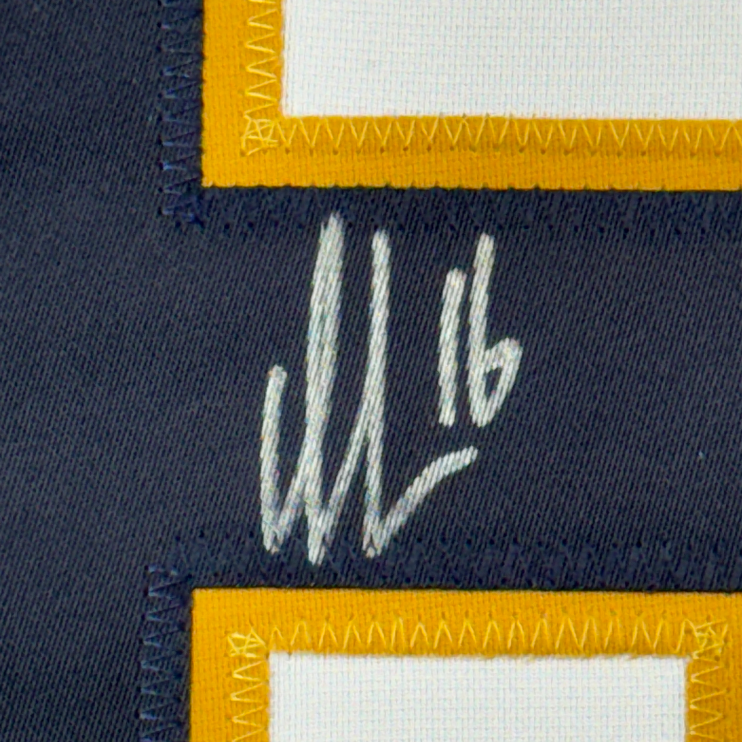 Close-up of handwritten signature in white ink on dark navy fabric between yellow and white striped borders.