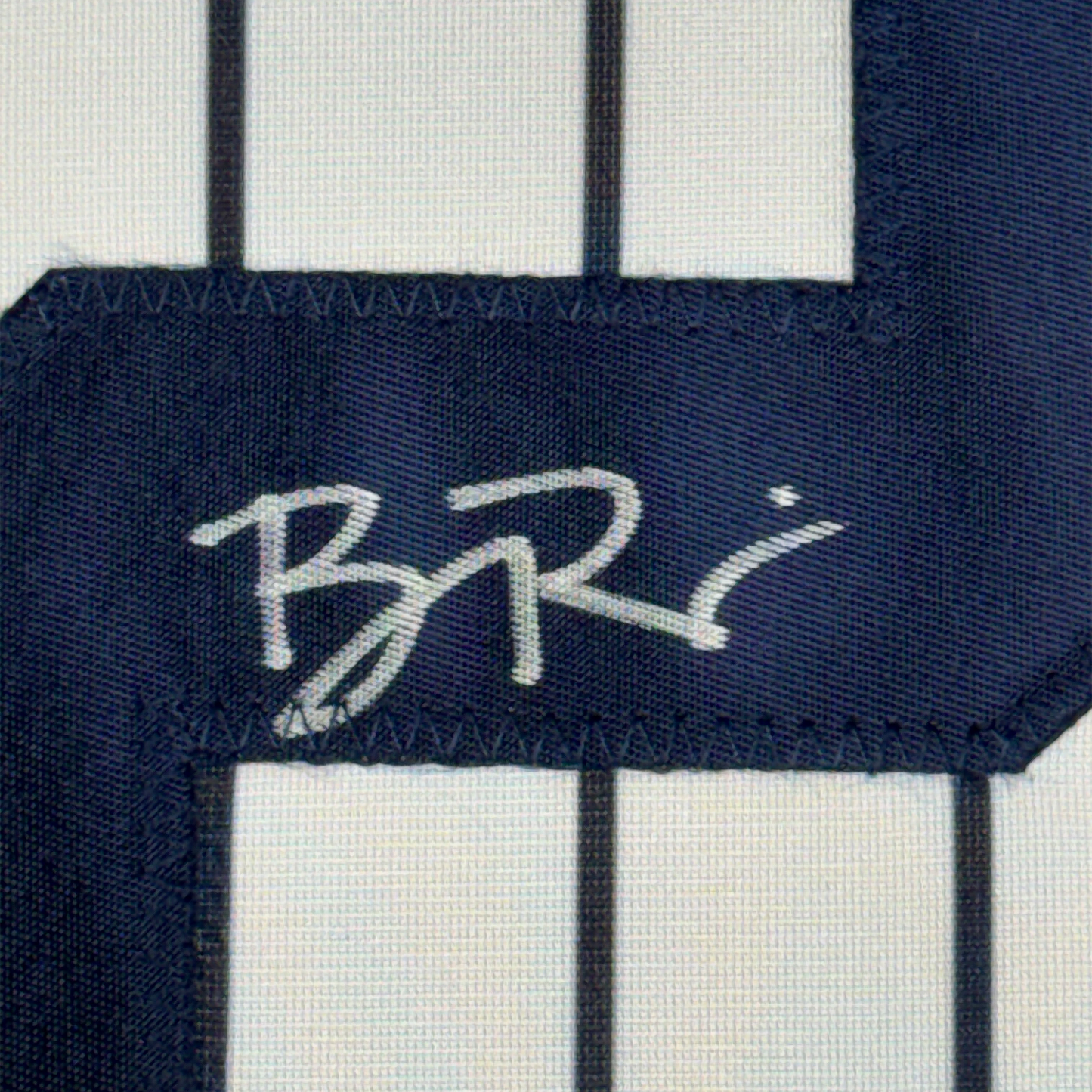 Close-up of autographed navy pinstripe baseball jersey fabric showing white signature on dark blue stripe.