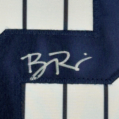 Close-up of autographed navy pinstripe baseball jersey fabric showing white signature on dark blue stripe.