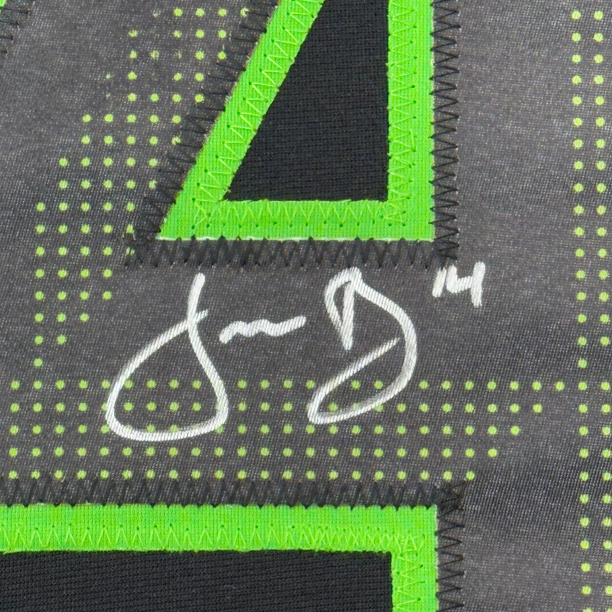 Close-up of neon green binding trim and white signature on dark grey jersey fabric with yellow dot pattern.