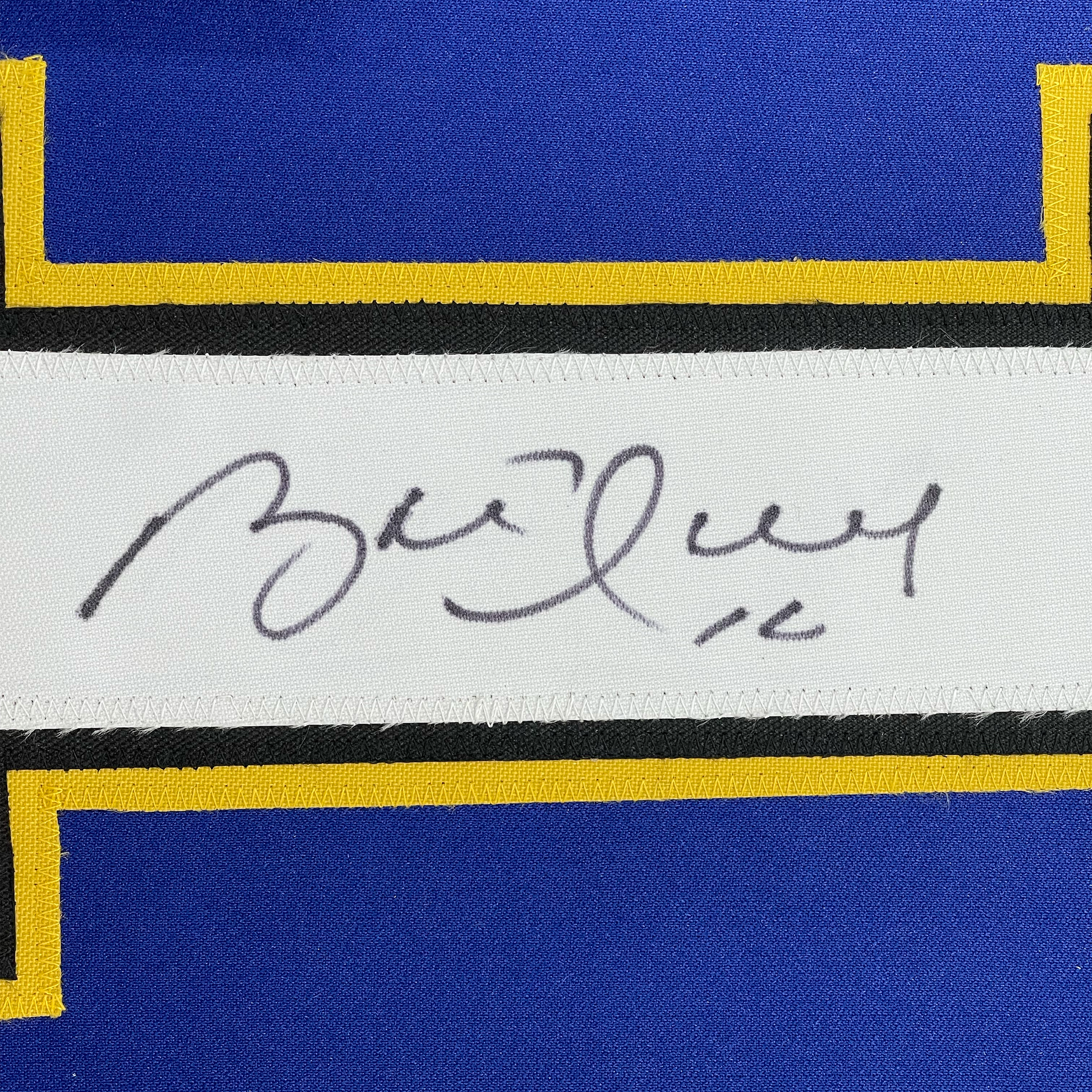 Close-up of handwritten signature on white label strip between blue and yellow striped jersey fabric.