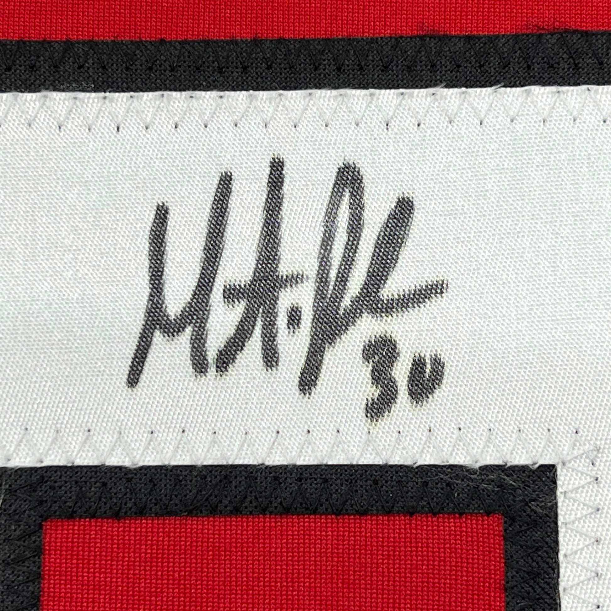 Close-up of Martin Brodeur's handwritten signature in black ink on white fabric with red and black striped jersey trim.