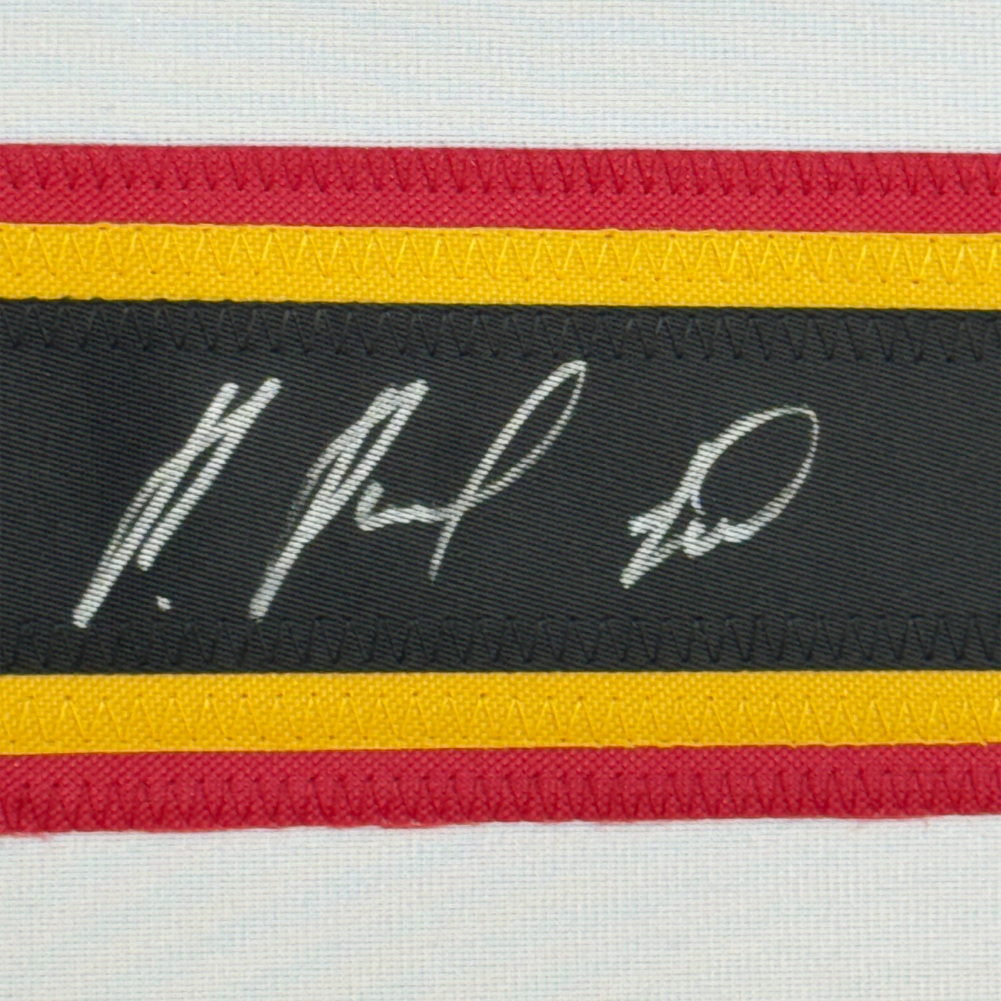 Close-up of horizontal striped fabric trim with handwritten signature on black stripe between red, yellow, and white bands.