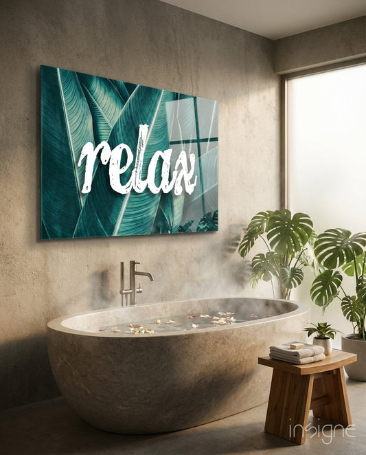 Glass wall art with white "Relax" script over teal banana leaves, displayed above a stone bathtub in a spa bathroom.