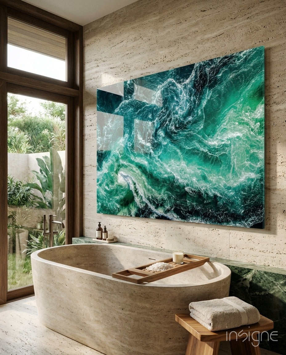 Turquoise ocean waves glass wall art displayed above a stone bathtub in a modern bathroom with travertine walls.