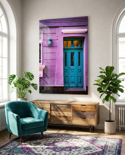 Purple House Glass Wall Art displayed above wooden dresser in bright room with teal chair and potted plants.