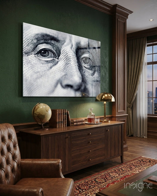 Glass wall art displaying close-up engraved banknote portrait eyes in black and white, mounted above wooden desk in green study.