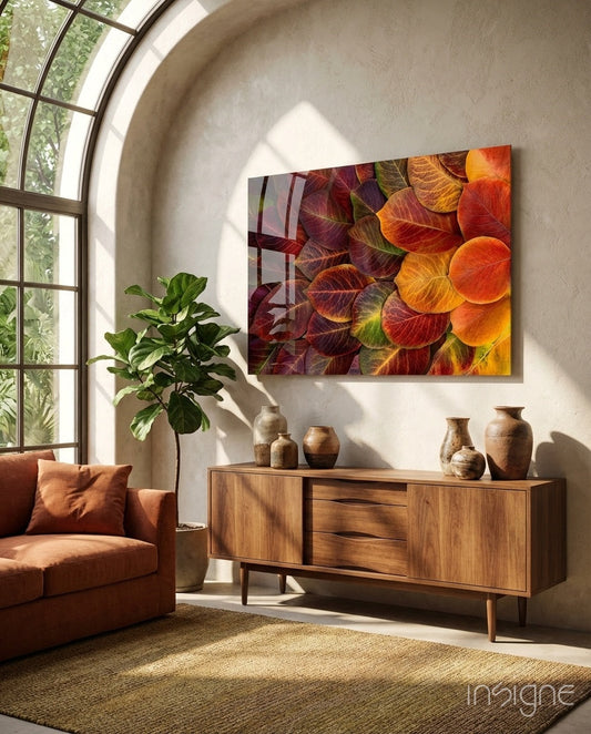 Orange Leaves Glass Wall Art hanging above wooden mid-century sideboard in sunlit living room with terracotta chair and potted plant.