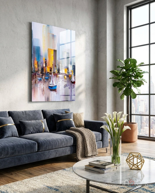 Colorful abstract harbor sailboat cityscape glass wall art hanging above a blue sofa in a modern living room with large windows.