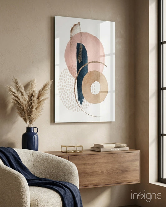 Abstract glass wall art featuring blush, navy, and gold geometric rings and dots displayed above wooden furniture in a styled interior.
