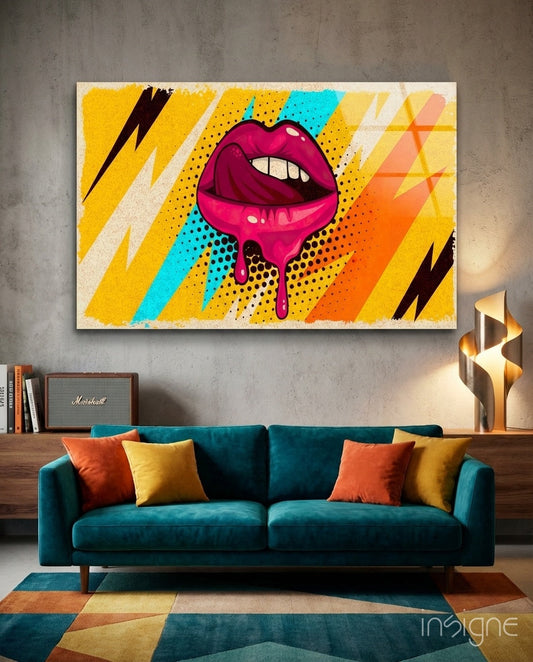 Vibrant pop art glass wall art featuring magenta dripping lips with yellow, cyan, and orange lightning bolts and geometric patterns displayed above a teal sofa.