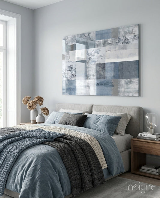 Blue geometric patchwork glass wall art hanging above beige upholstered bed with blue bedding and knit throw blanket.