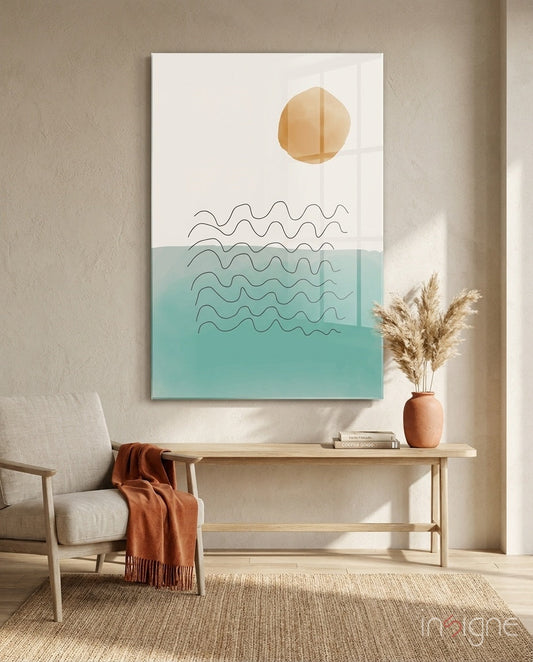 Modern minimalist glass wall art featuring an ochre sun and teal ocean waves above a wooden console in a neutral interior.