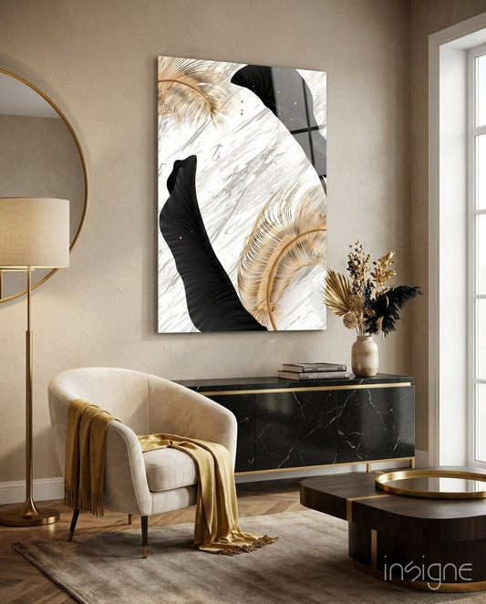 Gold feather and black leaf marble glass wall art displayed above a black dresser in a contemporary living room setting with cream chair and brass accents.