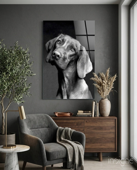 Black and white dog portrait glass wall art displayed above wooden dresser in modern gray interior setting with chair and plants.
