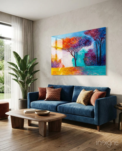 Colorful glass wall art depicting autumn trees in blues, oranges, and purples displayed above a blue sofa in a modern living room.