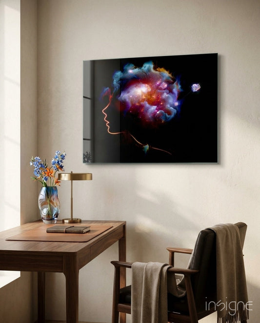 Glass wall art depicting glowing profile with colorful nebula brain displayed above wooden desk with flowers and brass lamp.