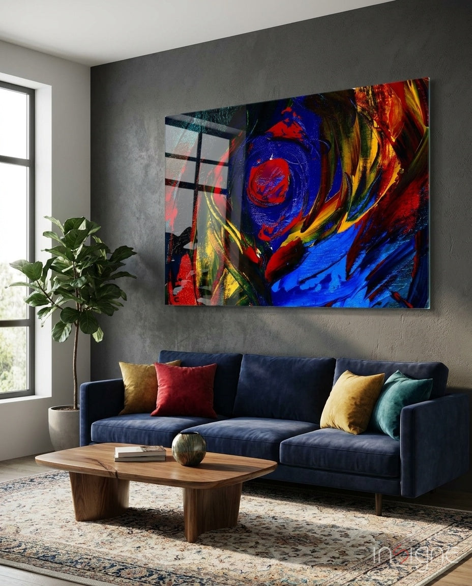 Vibrant abstract oil painting glass wall art with red, blue, and yellow swirls displayed above navy sofa in modern living room.