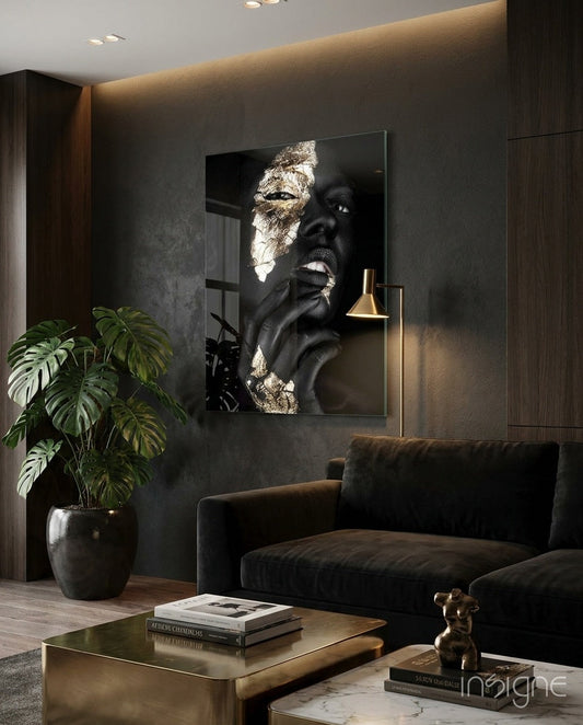 Black and gold glass wall art portrait displayed above dark sofa in modern luxury interior with marble coffee table.
