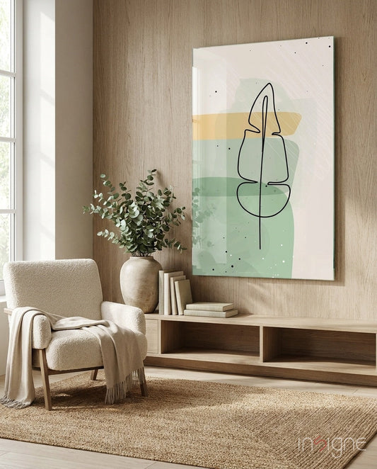 Modern living room with beige armchair, wooden low console, potted eucalyptus, and large glass wall art featuring minimalist line-drawn leaf in black with watercolor yellow and green washes.